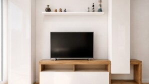 A modern living room with a flat-screen TV on a wooden stand, a white shelf with decorative items, and a minimalist design. - 🏖Sea views + private beach. What else? (Tossa de Mar)