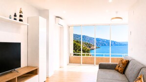 A modern living room with a flat-screen TV, a grey sofa with patterned cushions, and a large window offering a coastal view. - 🏖Sea views + private beach. What else? (Tossa de Mar)