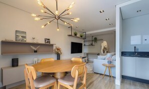 A modern living room with a round wooden dining table, two wooden chairs, a ceiling light fixture, a mounted TV, and a sofa. - Building With Swimming Pool Next to Balneario Shopping in BC - TSO (Balneário Camboriú)