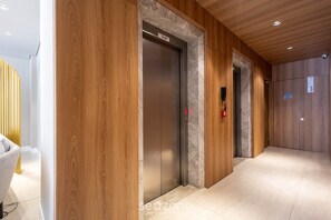 A hallway with wooden paneling, an elevator, and a sign indicating 'Social' on the elevator. - Building With Swimming Pool Next to Balneario Shopping in BC - TSO (Balneário Camboriú)
