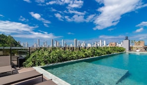 A rooftop pool with clear blue water, surrounded by lush green plants and overlooking a city skyline. - Building With Swimming Pool Next to Balneario Shopping in BC - TSO (Balneário Camboriú)