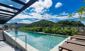 Una piscina sul tetto con acqua cristallina, circondata da lussureggiante vegetazione e vista su una collina boscosa.
