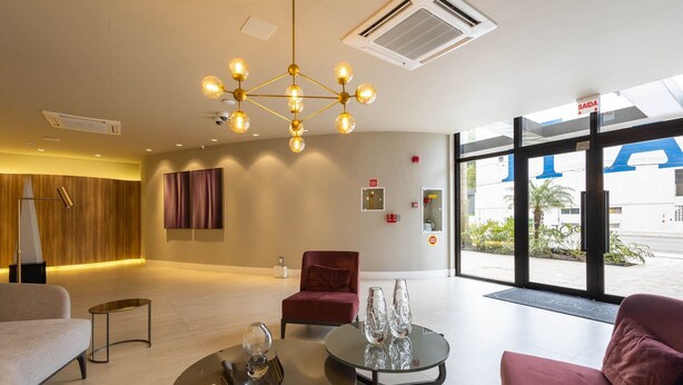 Un hall d’entrée moderne avec un lustre central, un fauteuil rouge et une table en verre agrémentée d’objets décoratifs.