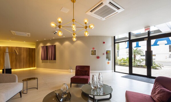A modern lobby with a central chandelier, a red chair, and a glass table with decorative items. - Building With Swimming Pool Next to Balneario Shopping in BC - TSO (Balneário Camboriú)