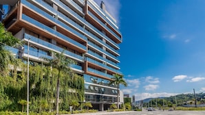 Un hôtel à plusieurs étages, doté de balcons, entouré de verdure et surplombant un ciel dégagé.