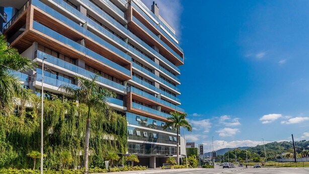 Un hôtel à plusieurs étages, doté de balcons, entouré de verdure et surplombant un ciel dégagé.