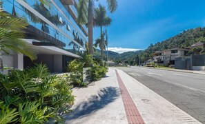 Un edificio moderno con facciata in vetro, un marciapiede con pavimentazione tattile e una strada con veicoli.