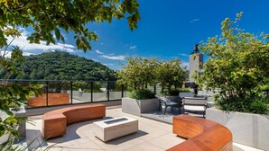 Une terrasse sur le toit, dotée de sièges aux lignes courbes, d’une table basse et offrant une vue sur une colline boisée.
