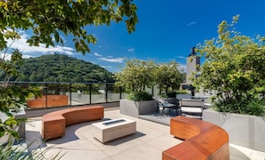 A rooftop terrace with curved seating, a coffee table, and a view of a forested hill. - Building With Swimming Pool Next to Balneario Shopping in BC - TSO (Balneário Camboriú)