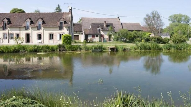 Une rangée de maisons traditionnelles, avec un étang au premier plan.