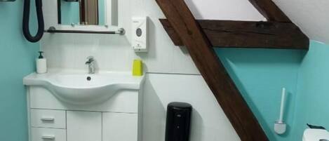A bathroom with a white sink, mirror, and toilet, wooden beams, and a patterned rug.