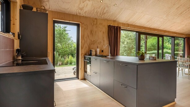 A modern kitchen with a central island, wooden ceiling, and large windows offering a view of the outdoors.