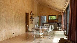A spacious room with a wooden interior, a dining table with chairs, a kitchen area with a window, and a large sliding door.