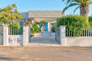 Une entrée fermée par un portail, avec un chemin pavé menant à un bâtiment doté d’une porte bleue et d’une plaque portant le numéro « 22 ».