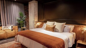 A modern hotel room with a large bed, a sofa, a potted plant, and a nightstand with a lamp. - The Host Medellin  (Medellín)