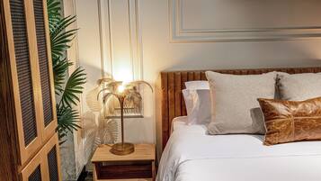 Un dormitorio ordenado con cama, almohadas, mesita de noche, lámpara y una planta en maceta.