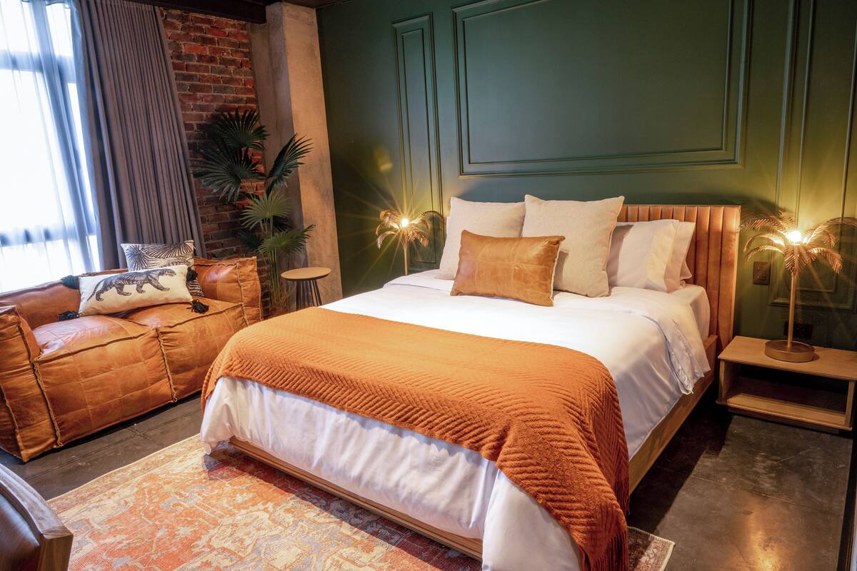 Een slaapkamer met een groot bed, een bank en een nachtkastje met een lamp.