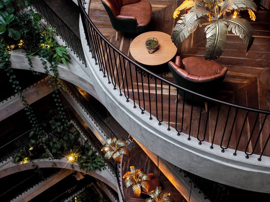 Un interior de varios niveles con una escalera de caracol central, zonas de estar con sofás de cuero y luminarias decorativas con motivos de hojas.