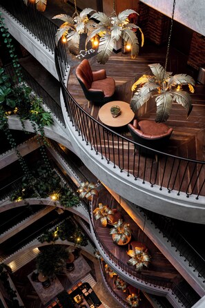 Un interior de varios niveles con una escalera de caracol central, zonas de estar con sofás de cuero y luminarias decorativas con motivos de hojas.