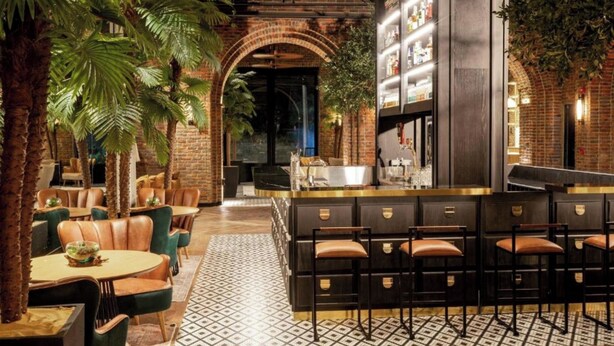 Uma área de estar interna com mesas, cadeiras, um balcão de bar e uma parede de tijolos.