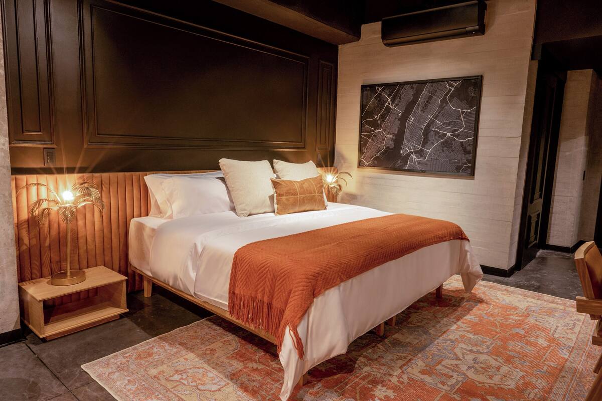 Een net opgemaakt bed met een wit-oranje deken, twee bedlampen en een grote kaart aan de muur.
