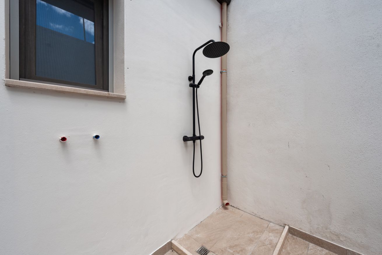 Ein Zimmerteil mit einer Dusche, einem Fenster und einer Wandrohrleitung.