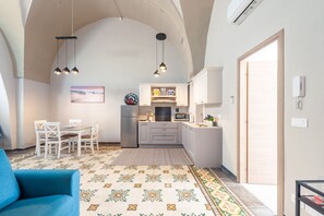 Un espacio habitable compacto con comedor, kitchenette y un sofá azul.