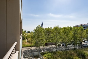 A view from a balcony overlooking a parking lot with trees, a building with a tower, and a clear sky.