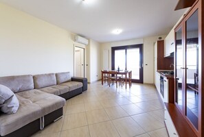 Un salon avec un canapé, une table à manger avec des chaises, un coin cuisine avec des placards et une porte-fenêtre coulissante.