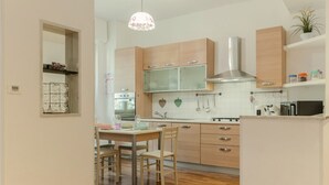 A kitchen with wooden cabinets, a stainless steel range hood, a dining table with chairs, and a pendant light. - GuestHost - Cozy 90 sq m apartment, able to accommodate up to 6 people, located on the 1st floor of a building with an elevator (there are STEPS to access it). The apartment is located in the Migliarina district, a well-served and quiet residential area, (La Spezia)