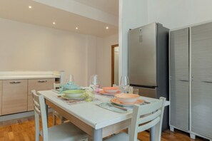 A modern kitchen with a dining table set for four, a refrigerator, and a wardrobe.