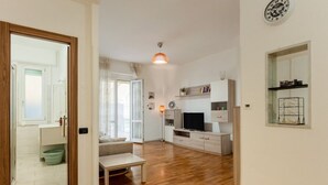 A modern living room with a wooden floor, a sofa, a coffee table, a TV, and a dining area with a table and chairs. - GuestHost - Cozy 90 sq m apartment, able to accommodate up to 6 people, located on the 1st floor of a building with an elevator (there are STEPS to access it). The apartment is located in the Migliarina district, a well-served and quiet residential area, (La Spezia)