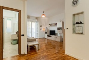 Ein modernes Wohnzimmer mit Holzboden, einer Couch, einem Couchtisch, einem Fernseher und einem Essbereich mit Tisch und Stühlen.