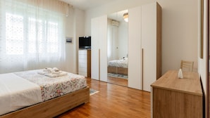 A bedroom with a wooden bed, a bedside table, a mirror, and a TV. - GuestHost - Cozy 90 sq m apartment, able to accommodate up to 6 people, located on the 1st floor of a building with an elevator (there are STEPS to access it). The apartment is located in the Migliarina district, a well-served and quiet residential area, (La Spezia)