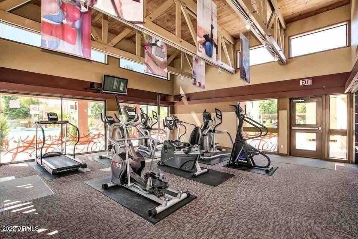 Een fitnessruimte met loopbanden, elliptische trainers en krachttrainingsapparaten. Er hangt een televisie aan de muur en er is een vluchtwegbord.