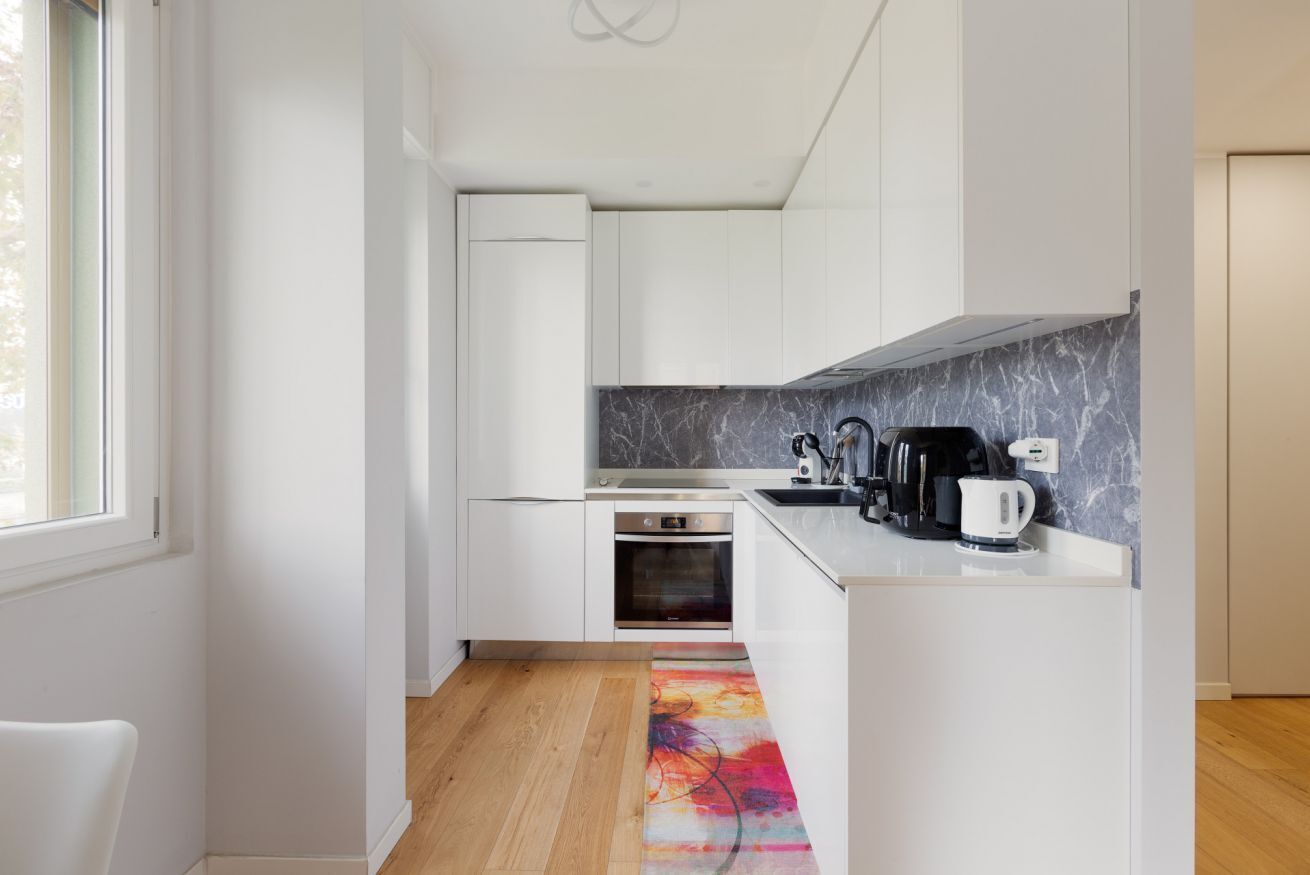 A modern kitchen with white cabinets, a marble backsplash, and a coffee maker on the counter.