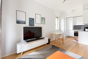 A modern living room with a flat-screen TV, a dining area, and a kitchen.
