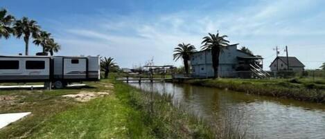 Een grasveld met een waterweg, een caravan en een gebouw met een schuin dak.