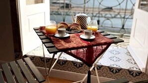 Ein Frühstückstisch auf einem Balkon mit Tassen, einem Teekessel und einer Platte Pfannkuchen.