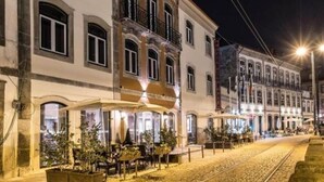 Eine historische Straße mit Gebäuden mit Rundbogenfenstern und Balkonen, Kopfsteinpflaster und Außenbereichen mit Sitzgelegenheiten.