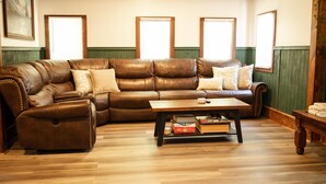 A living room with a brown leather sectional sofa, a wooden coffee table, and a green wainscotted wall.