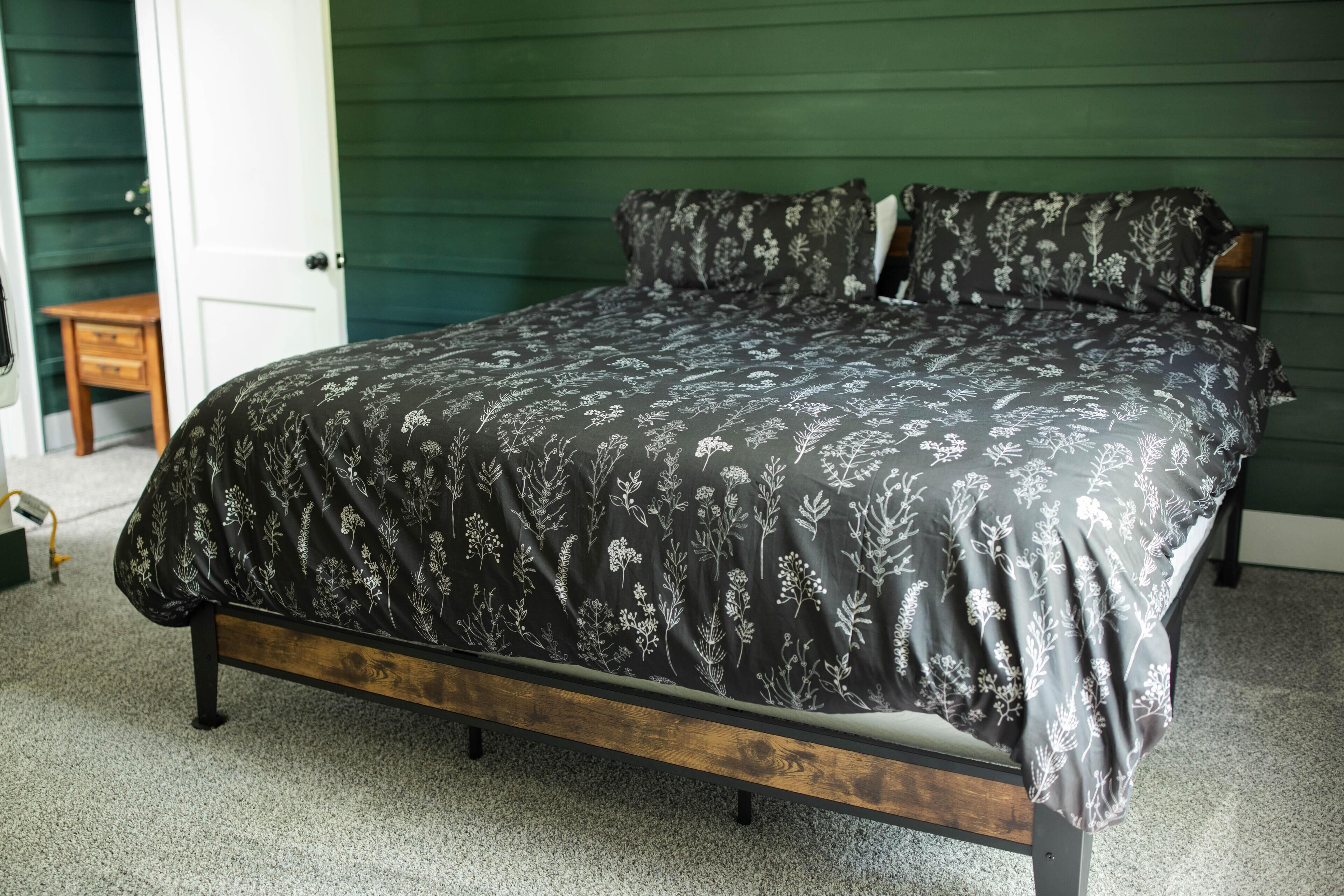 Uma cama com colcha estampada em um quarto com paredes verdes e piso de madeira.