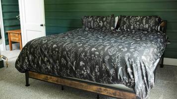 Uma cama com colcha estampada em um quarto com paredes verdes e piso de madeira.