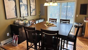 A dining area with a large wooden table, four chairs, a chandelier, and three framed maps on the wall.