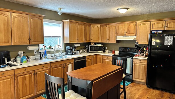 A kitchen with wooden cabinets, a black refrigerator, a coffee maker, and a dining table with chairs.