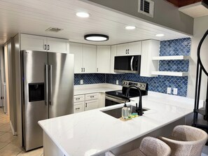 Uma cozinha moderna com armários brancos, eletrodomésticos de aço inoxidável, micro-ondas preto e painel de azulejos azuis.