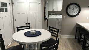 A kitchen with a round table, chairs, a clock, and a washer and dryer. - Algonac Harbour House (Algonac)
