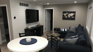 A modern living room with a round dining table, black chairs, a dark blue sofa, and a flat-screen TV mounted on the wall. - Algonac Harbour House (Algonac)