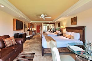 A hotel room with a sofa, two beds, a dining area, and a TV.