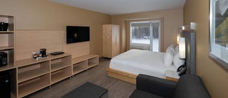 A modern hotel room with a bed, a TV, a desk, and a sofa.